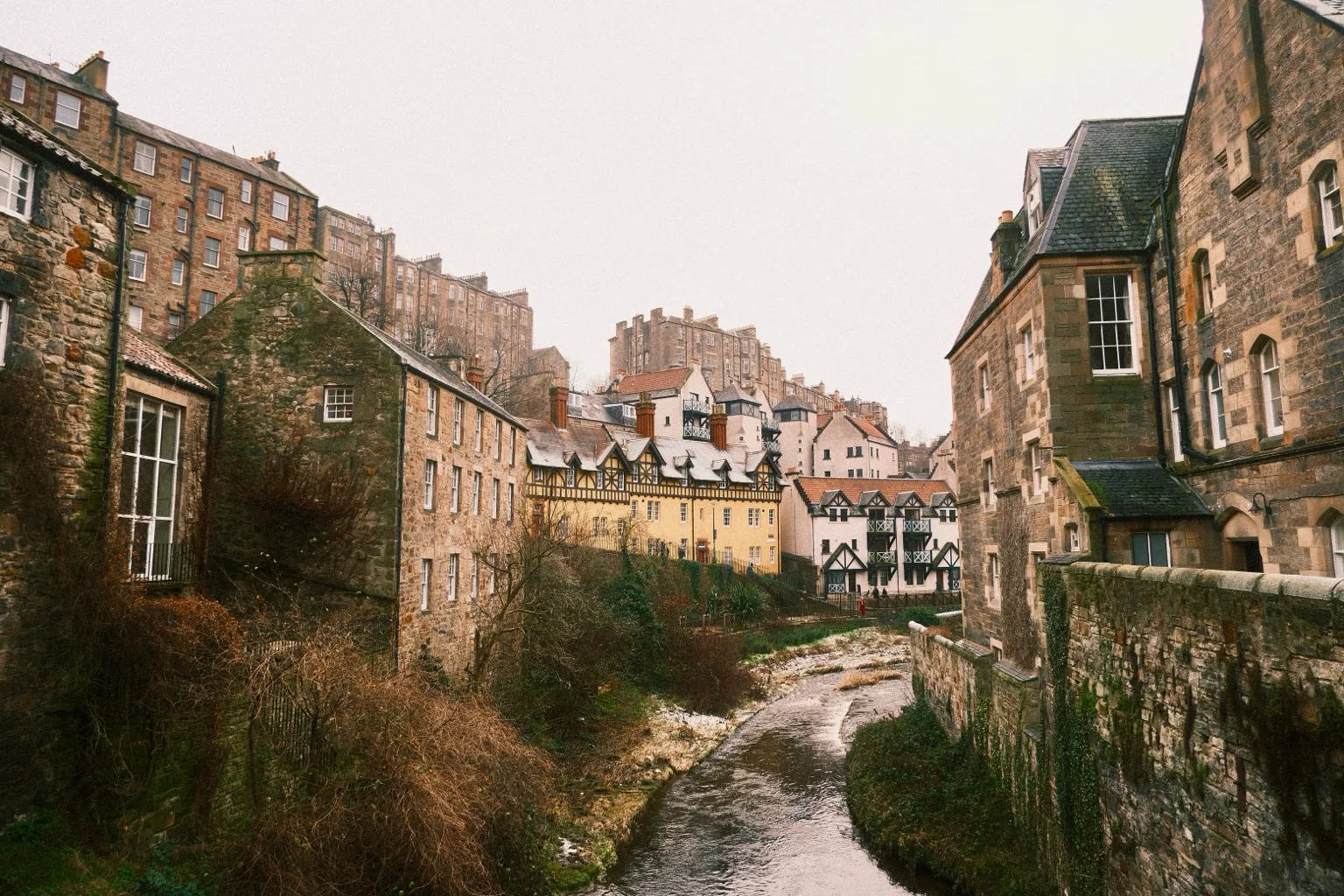Historic stone buildings with steep roofs and chimneys rising above the Water of Leith in Dean Village, Edinburgh.